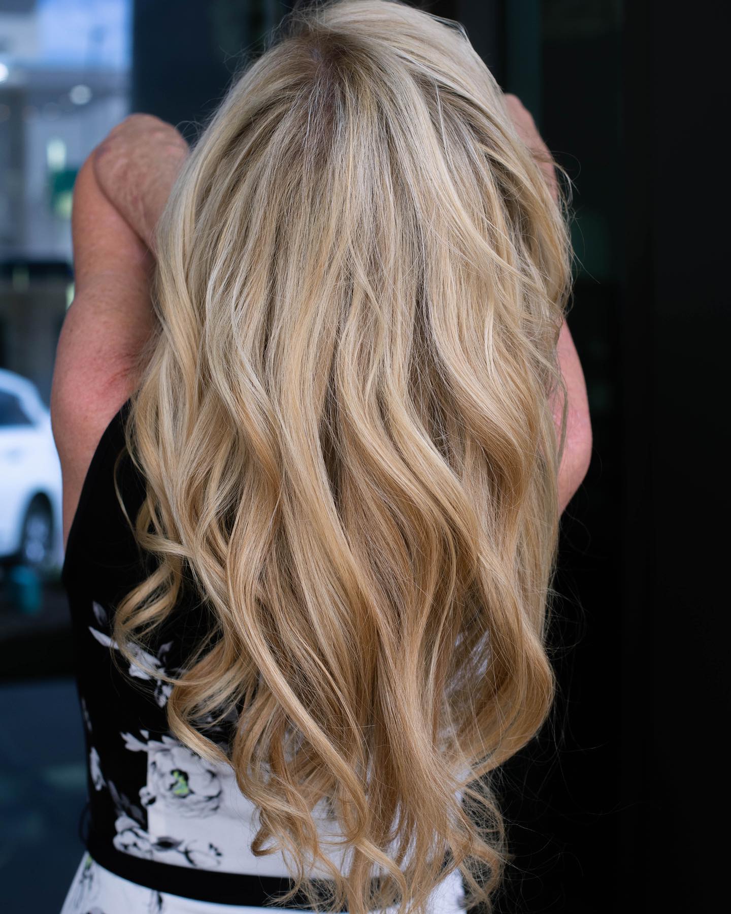 A person with long, wavy blonde hair seen from behind, wearing a black and white patterned top—capturing the look often found at a premier salon Naples known for expert hair color extensions facials nails. Zen Aveda Salon in Naples, FL