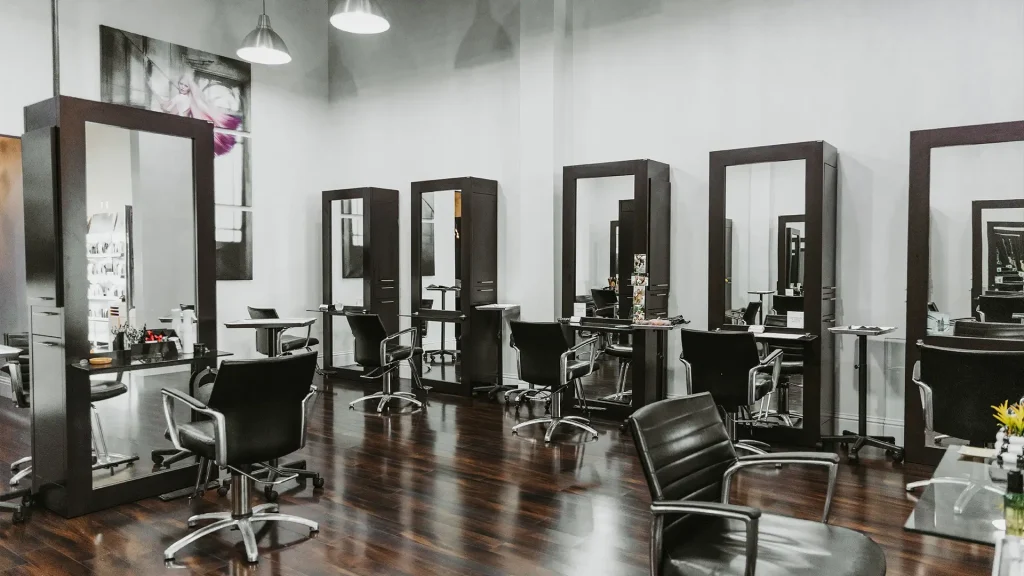 A modern Aveda hair salon with multiple styling stations, black chairs, large mirrors, and dark wood flooring under bright ceiling lights—experience the best salon Naples FL has to offer. Zen Aveda Salon in Naples, FL