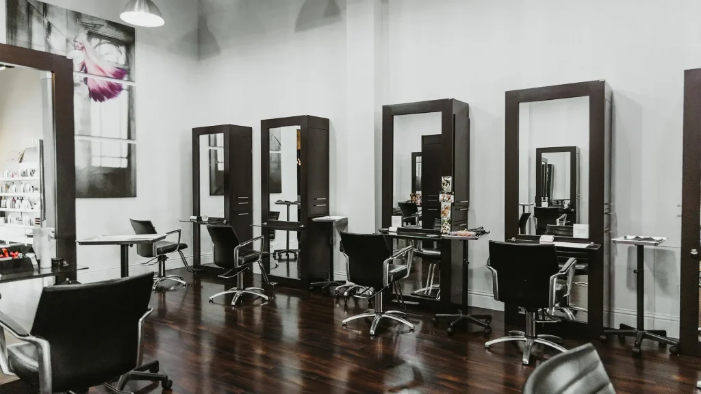 A modern Aveda hair salon interior with several black styling chairs, large mirrors, dark wooden floors, and minimal decor—experience one of the best salon Naples FL locations for exceptional style. Zen Aveda Salon in Naples, FL